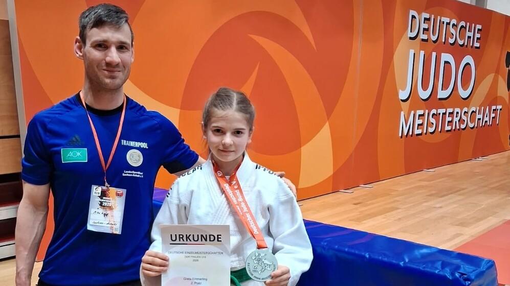 Alexander Lenk und Greta Emmerling Alexander Lenkt steht neben Greta Emmerling die eine Urkunde über den zweiten Platz sowie eine Medaille hochhält.