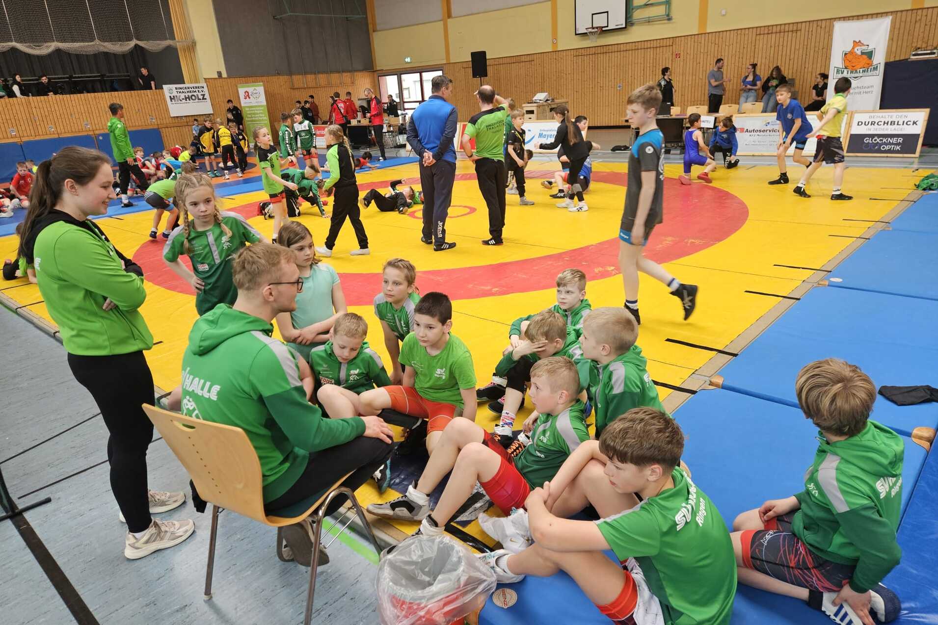 Impression Wettkampf Thalheim Der Ringernachwuchs sitz auf einer Matte und hört dem Trainer zu.