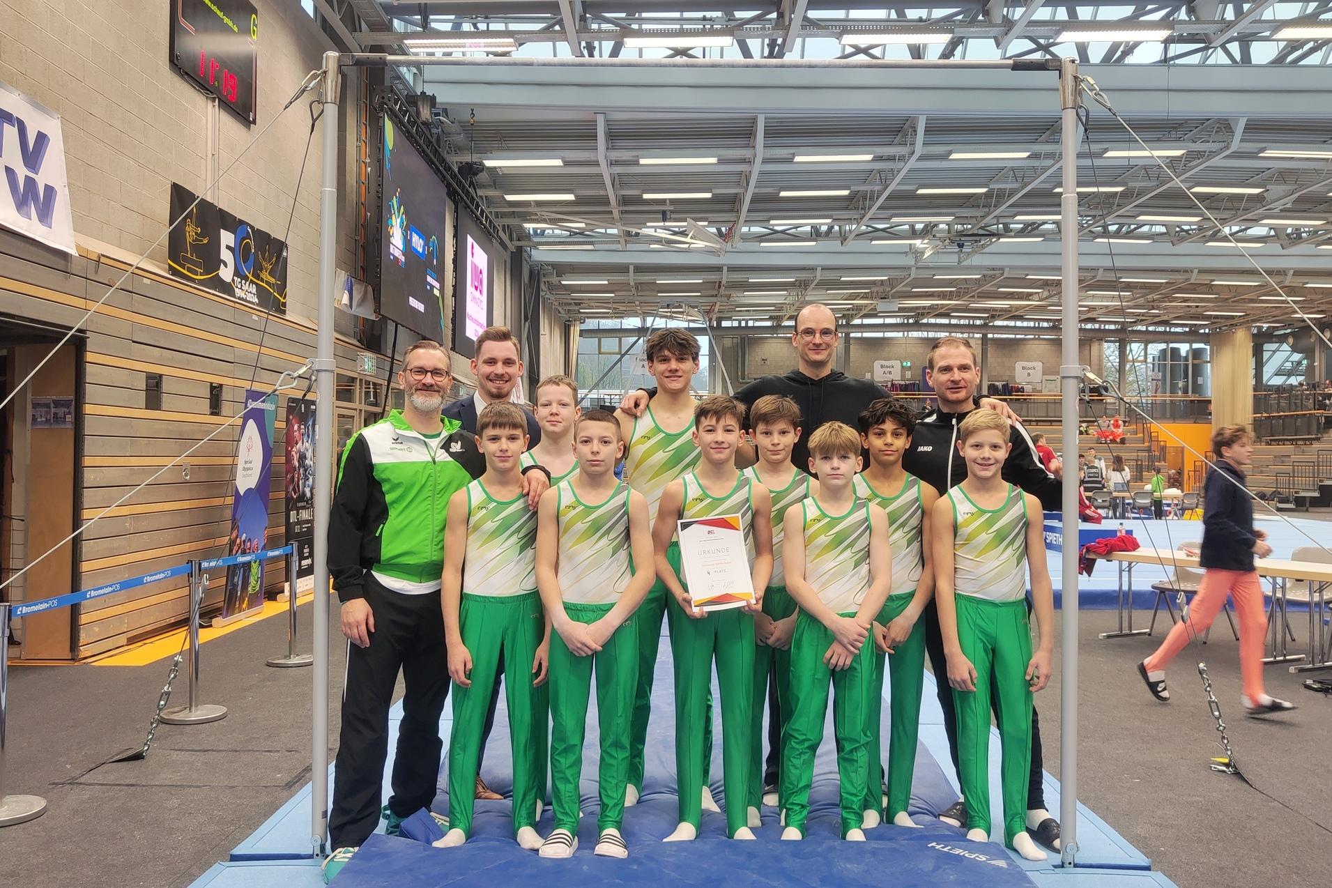 Gruppe von Jungen in Sportkleidung und Trainern, posierend mit einer Urkunde an einem Gymnastikgerüst.