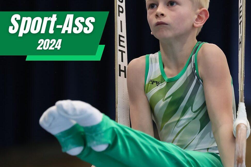 Junge in sportlicher Kleidung übt an Turnringen, sitzt in Gleitposition mit konzentriertem Gesichtsausdruck.